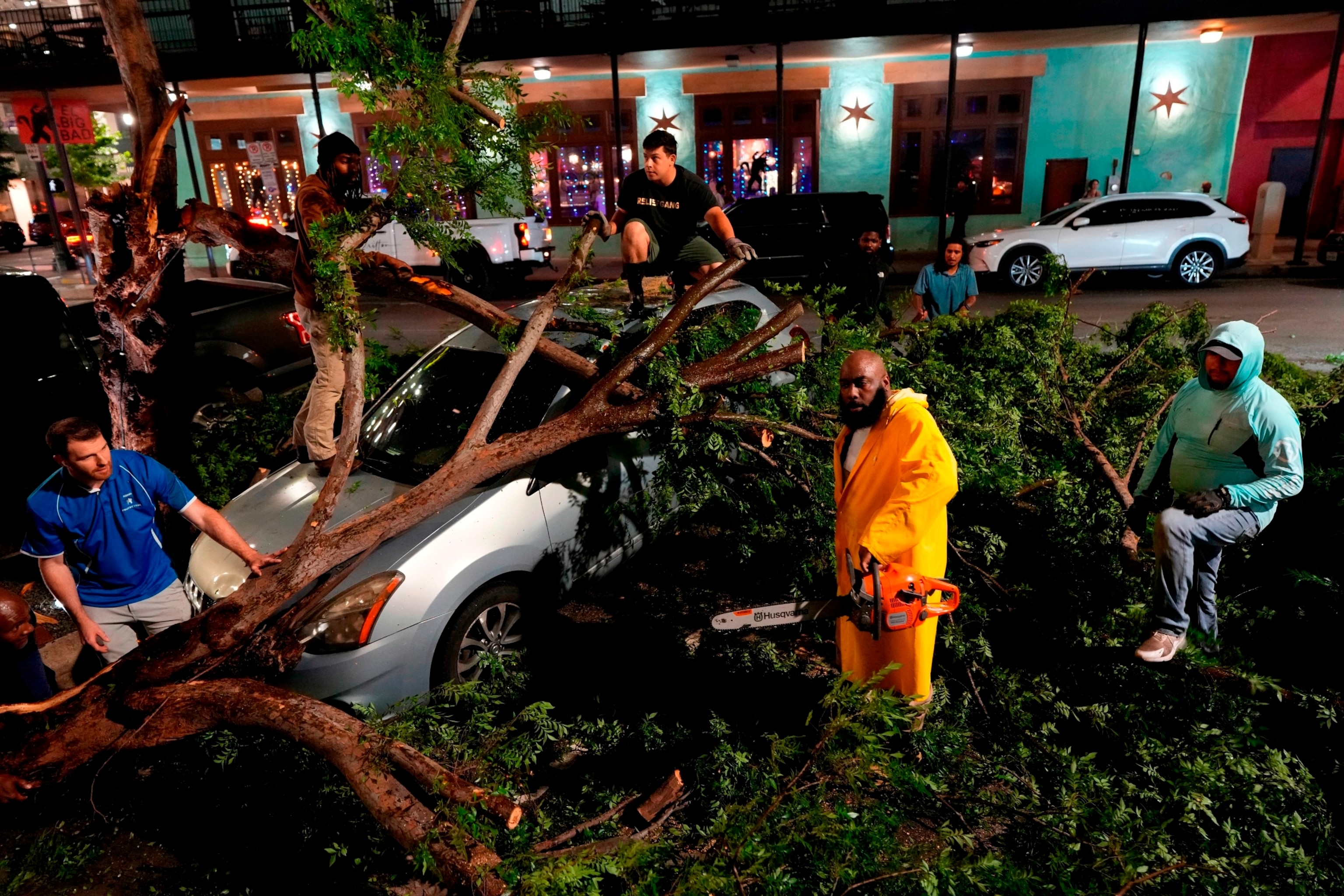 PHOTO: Rapper Trae tha Truth, in yellow, cuts fallen tree limbs on top of a car in the aftermath of a severe thunderstorm that passed through downtown, May 16, 2024, in Houston. 