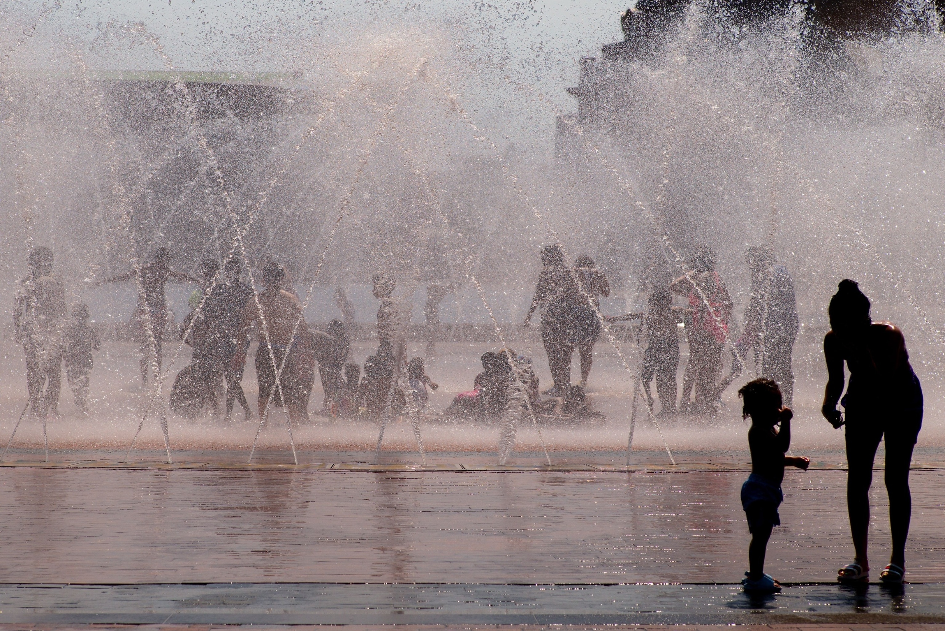 PHOTO: A woman attends to a young child at the edge of the water fountain on the Christian Science Plaza while others escape the heat in the water, in Boston, June 19, 2024.