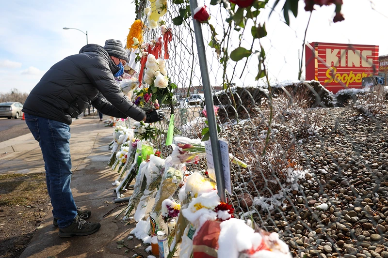 A man places flowers in the fence at a makeshift memorial for the victims of a mass shooting outside a King Soopers grocery store on March 24, 2021 in Boulder, Colorado. Ten people, including a police officer, were killed in the shooting on Monday.(Photo by Michael Ciaglo/Getty Images)