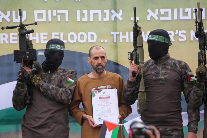 TOPSHOT - CORRECTION / Hamas fighters escort Israeli hostage Eli Sharabi on a stage before handing him over to a Red Cross team in Deir el-Balah, central Gaza, on February 8, 2025. Hamas militants handed over three Israeli hostages on February 8, as part of the fifth exchange under a fragile Gaza ceasefire, with 183 prisoners held by Israel due to be released later in the day. (Photo by Eyad BABA / AFP) / "The erroneous mention[s] appearing in the metadata of this photo by Eyad BABA has been modified in AFP systems in the following manner: [Eli Sharabi] instead of [Or Levy]. Please immediately remove the erroneous mention[s] from all your online services and delete it (them) from your servers. If you have been authorized by AFP to distribute it (them) to third parties, please ensure that the same actions are carried out by them. Failure to promptly comply with these instructions will entail liability on your part for any continued or post notification usage. Therefore we thank you very much for all your attention and prompt action. We are sorry for the inconvenience this notification may cause and remain at your disposal for any further information you may require." (Photo by EYAD BABA/AFP via Getty Images)